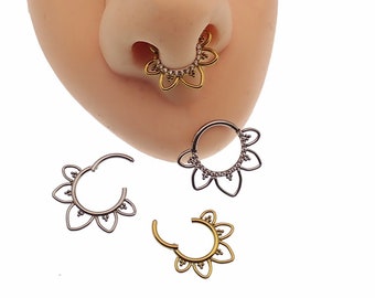 Op de afbeelding: Gouden en zilverkleurige septumringen met een bloemmotief. De ringen zijn versierd met kleine, heldere edelstenen. Eén ring wordt op een neus getoond, terwijl de andere afzonderlijk worden weergegeven. De ringen hebben een scharniersluiting.