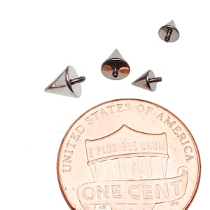 May include: Four silver cone-shaped body jewellery pieces with a threaded post. The jewellery is shown next to a US penny for size comparison.