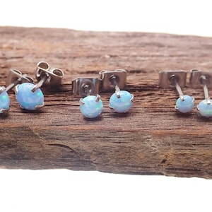 May include: A set of three pairs of silver stud earrings with light blue opal stones.