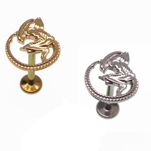 May include: Two metal labret studs. One is gold-toned, the other silver-toned. Each features a detailed alien design within a circular frame. The studs have a flat back and a threaded post for secure wear. Ideal for body piercings.