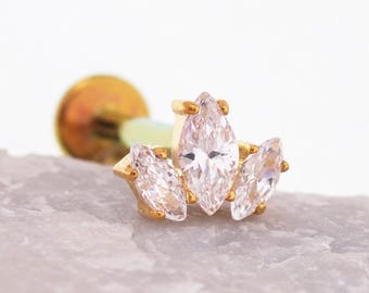 May include: A gold-toned flat back stud earring featuring three marquise-cut clear stones arranged in a fan-like cluster. The central stone is larger than the two flanking stones, all held in place by small gold prongs on a metal post base.