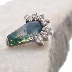 Op de afbeelding: Een zilveren ring met een groene mosagaat-steen en een halo van kleine heldere diamanten.