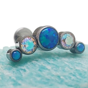 May include: A silver body jewelry piece with five blue and iridescent gemstones. The gemstones are arranged in a curved line.