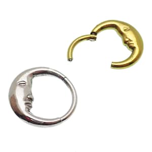 May include: Two crescent moon shaped body jewelry pieces. One is silver and the other is gold. Both have a face on the crescent.