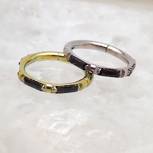 May include: Two seamless hoop earrings with a black and gold design. The hoop earrings are made of metal and have a hinged closure.