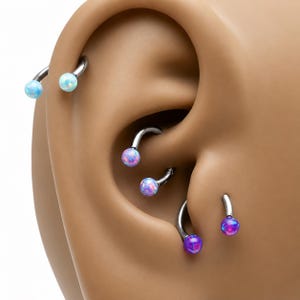 May include: Three curved barbell piercings with metallic silver bars and spherical ends. The top pair features light blue opal-style beads, the middle pair has light purple beads, and the bottom pair displays vibrant dark purple opal-style beads.