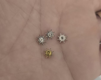 Puede incluir: Cuatro pequeños abalorios en forma de sol, en tonos plateados y dorados. Los abalorios tienen un círculo central con puntas radiantes, que se asemejan a un sol estilizado. Pequeñas dimensiones, para joyería o manualidades.