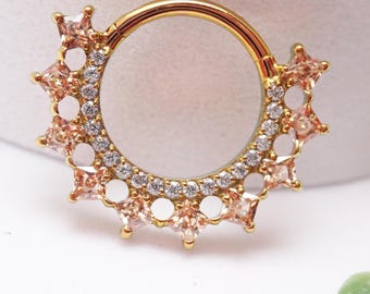May include: A gold-toned circular hoop ring featuring a decorative sunburst design. The outer edge is adorned with alternating square-cut peach-colored gemstones and small clear white crystals, creating a radiant and detailed jewelry piece.
