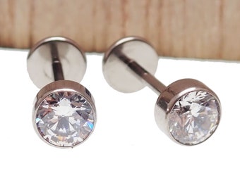 May include: Two silver-colored, stud earrings with a clear, sparkling, round-cut cubic zirconia stone. The earrings have a flat back and a post for piercing. The setting is a bezel style, which holds the stone securely.