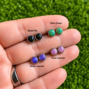 Può includere: Quattro paia di orecchini a lobo rotondi con cabochon in opale sintetico nei colori black fire, olive green, royal lavender e sleepy lavender, incastonati in una semplice montatura in metallo, con etichette che identificano ogni variante.