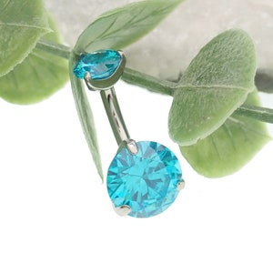 May include: A silver belly button ring with two turquoise blue gem stones. The larger gem stone is round and the smaller gem stone is teardrop shaped.