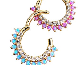 May include: Two gold-tone hinged segment rings featuring a row of clear cubic zirconia stones and a series of round cabochon stones. One ring displays pink cabochons, while the other ring displays light blue cabochons along the outer edge.