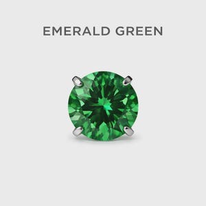 May include: A single, round emerald green gemstone with a faceted surface, set in a silver or white metal setting. The text "EMERALD GREEN" is displayed above the gemstone against a white background.