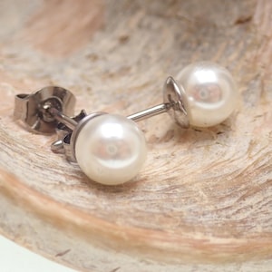 May include: A pair of stud earrings featuring round, white, lustrous pearls set on silver-toned metal posts. Each earring includes a matching silver-toned metal butterfly back closure, designed for secure attachment to the earlobe.