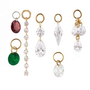 May include: A collection of gold-toned earrings with various gemstone and crystal designs. The earrings feature a range of shapes, including oval, teardrop, and diamond-shaped crystals, and a green and red gemstone.