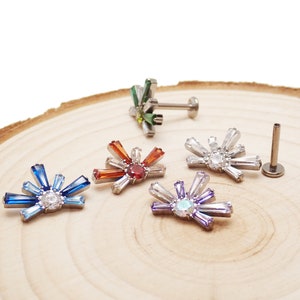 May include: Five different colored crystal sunburst body jewelry pieces. Each piece features a central round crystal surrounded by smaller crystals in a sunburst pattern. The jewelry is made of surgical steel and is available in a variety of colors.