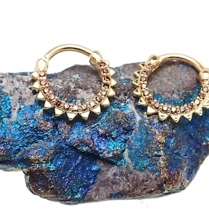 May include: Two gold-toned hoop earrings with a row of small pink gemstones and a row of gold spikes around the edge.