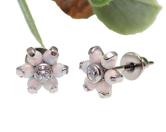 Könnte beinhalten: Ein Paar silberne Ohrringe in Blumenform mit weißen Opal-Steinen und einem klaren Kristall in der Mitte. Die Ohrringe haben einen Stift und einen Schmetterlingsverschluss.