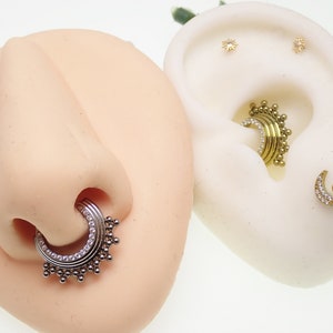 Pode incluir: Duas imagens de close-up de joias corporais. A primeira imagem mostra um anel de septo prateado com uma fileira de pequenas pedras transparentes e uma fileira de contas prateadas. A segunda imagem mostra uma piercing de cartilagem de orelha dourada com uma fileira de pequenas pedras transparentes e uma fileira de contas douradas.