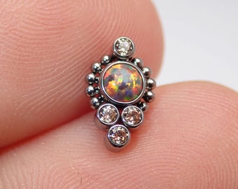 May include: A silver body jewelry piece with a cluster of clear gemstones and a central opal gemstone.