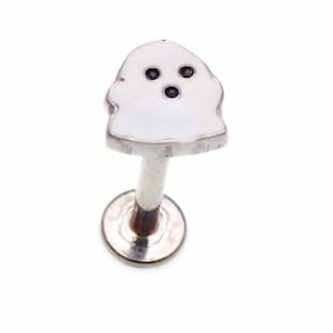 May include: A silver lip piercing featuring a white ghost design. The ghost has three black eyes and a simple, rounded shape. The piercing post and base are silver.