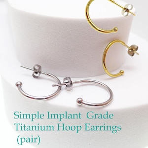 May include: Simple implant grade titanium hoop earrings in silver and gold. The earrings are a simple, minimalist design with a small ball at the end of the hoop. The text "Simple Implant Grade Titanium Hoop Earrings (pair)" is visible.