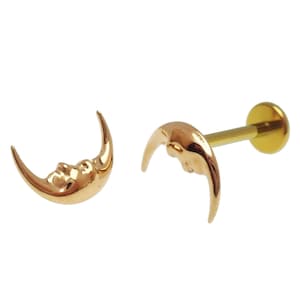 May include: Two gold-colored crescent moon-shaped earrings with a face carved into the moon's surface. One earring is a stud with a flat back and a post. The other earring is a standalone crescent moon.