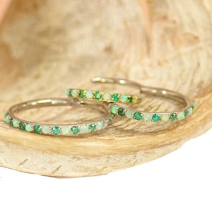 Puede incluir: Tres bandas finas de oro con una fila de peque&ntilde;as piedras preciosas verdes y blancas. Las bandas est&aacute;n apiladas una encima de la otra.