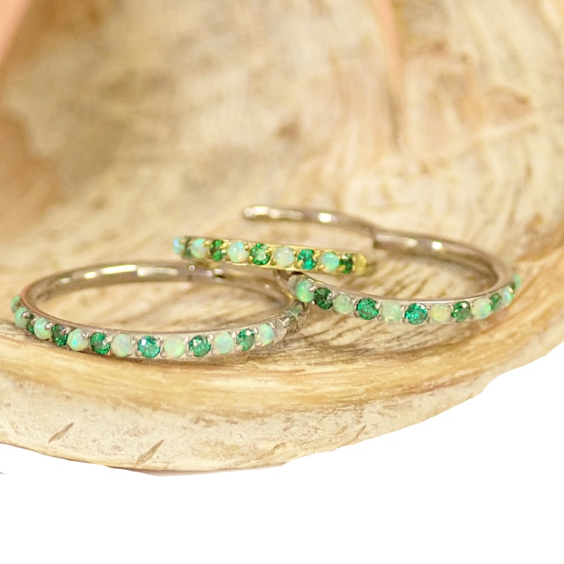 Puede incluir: Tres bandas finas de oro con una fila de peque&ntilde;as piedras preciosas verdes y blancas. Las bandas est&aacute;n apiladas una encima de la otra.