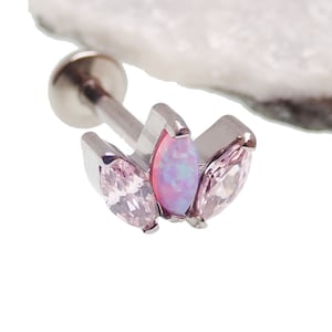 May include: A silver body jewelry piece with a pink opal and two pink marquise-shaped gems. The jewelry is a cartilage earring.