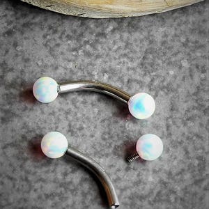May include: Two curved barbell body jewelry pieces made of polished silver-tone metal. Each end features a smooth, round, iridescent white opal-like bead. One barbell is fully assembled, while the other is shown with one bead detached, revealing the screw.