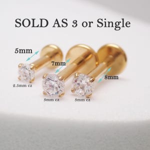 Könnte beinhalten: Drei goldfarbene Lippenpiercing-Stecker mit klaren kubischen Zirkonia-Steinen. Die Stecker sind 5 mm, 7 mm und 8 mm lang, mit 2,5 mm und 3 mm CZ-Steinen. Der Text "SOLD AS 3 or Single" steht oben.
