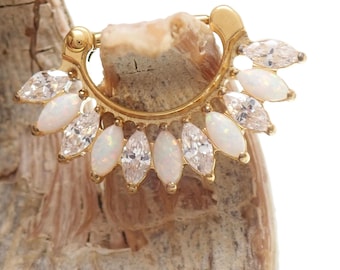 May include: Gold-toned septum ring featuring a half-circle design. The ring is adorned with alternating marquise-cut white opals and clear crystals, creating a sunburst effect. The jewelry is displayed against a neutral, textured background.