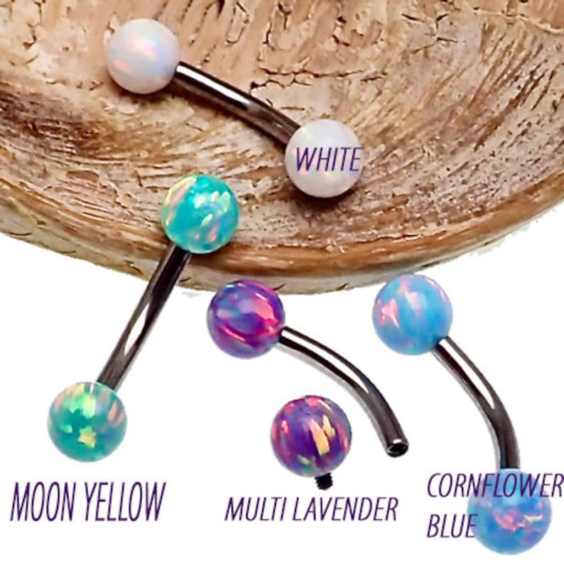 May include: A collection of curved barbell body jewelry pieces featuring iridescent opal-style spheres in white, moon yellow, multi lavender, and cornflower blue colors, each with a dark metallic curved shaft and threaded ball ends.