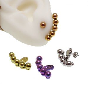 May include: Three pairs of ear cuffs with a row of small beads. The first pair is gold, the second is purple, and the third is silver.