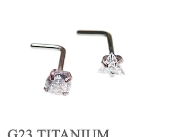 May include: Two titanium nose rings with clear cubic zirconia stones. One ring has a round stone and the other has a triangular stone. The rings are labelled "G23 TITANIUM".