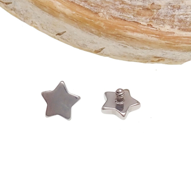 May include: Two silver-toned star-shaped jewelry components. One piece shows the flat, smooth front surface, while the other piece displays the back with a small, threaded metal post extending from the center for attachment purposes.