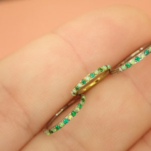 Puede incluir: Tres anillos de plata con una fila de piedras preciosas verdes y blancas. Los anillos est&aacute;n en el dedo de una persona.