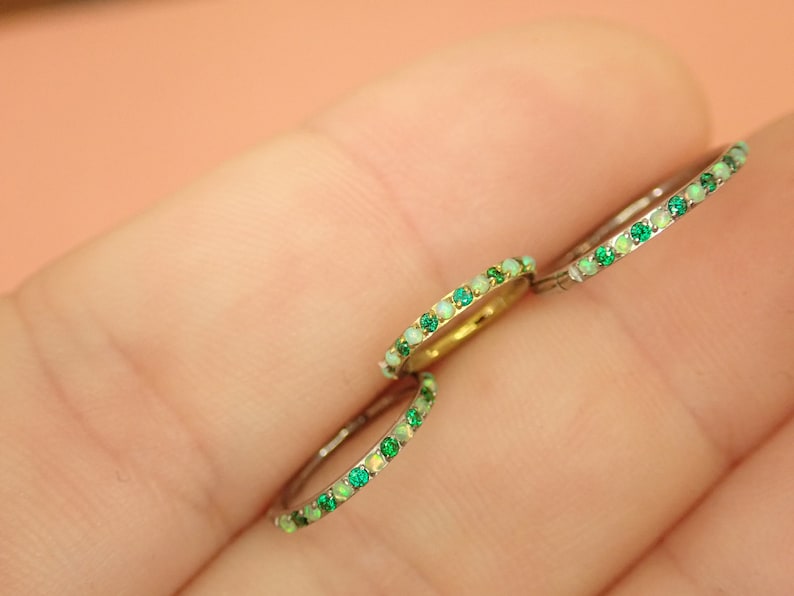 Puede incluir: Tres anillos de plata con una fila de piedras preciosas verdes y blancas. Los anillos est&aacute;n en el dedo de una persona.