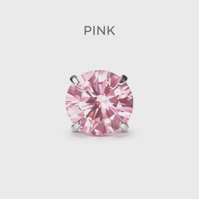May include: A single pink gemstone earring with a round cut, held by four silver prongs. The word "PINK" is displayed above the earring against a white background. The gemstone has a faceted surface.