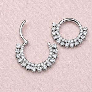 Peut inclure: Deux anneaux segmentés articulés de couleur argentée présentant un design incurvé orné de multiples cristaux ronds transparents. Les bijoux sont circulaires avec un mécanisme d'ouverture à charnière, affichant une rangée de pierres scintillantes.