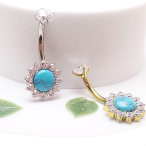 May include: Two belly button rings. One has a silver curved bar with a clear gem at the top and a turquoise stone surrounded by small clear gems at the bottom. The other has a gold curved bar.