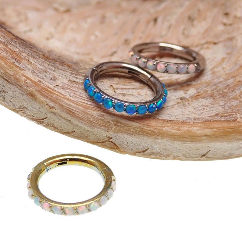 以下が含まれることがあります： 宝石のアクセントが付いた3つのフープピアス。1つのイヤリングは白い宝石が付いたゴールドトーン、別のイヤリングは青い宝石が付いたシルバートーン、3つ目は白い宝石が付いたシルバートーンです。イヤリングは木製の表面に表示されています。