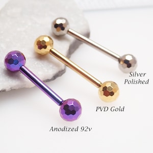 Könnte beinhalten: Drei Körperschmuckstücke: eines in Lila, eines in Gold und eines in Silber. Jedes hat eine facettierte Kugel an jedem Ende eines geraden Stabs. Das lila Stück ist mit "Anodized 92v" beschriftet, das goldene Stück mit "PVD Gold" und das silberne Stück mit "Silver Polished".