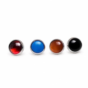 May include: Four circular stud earrings with a polished silver-tone metal rim. Each earring features a smooth, domed cabochon center in a different solid color: translucent red, opaque bright blue, translucent amber, and solid opaque black.