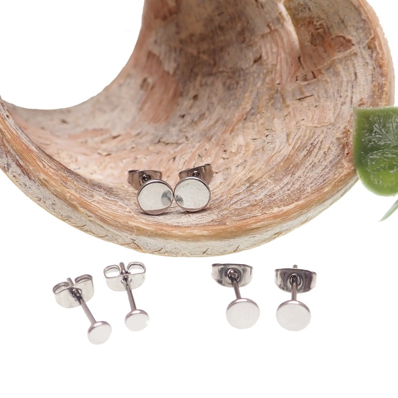 May include: Three pairs of silver stud earrings with round, flat fronts. The earrings are displayed on a wooden surface.
