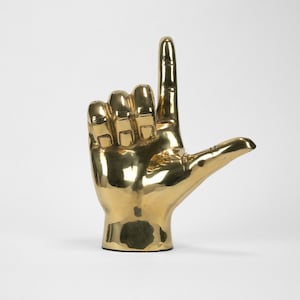 Escultura de latón con la letra "L" como signo de mano inicial
