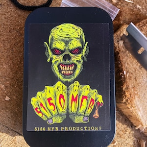 May include: Black metal box with a green and yellow sticker featuring a cartoon monster with red eyes and the text "5150 MFR PRODUCTIONS".