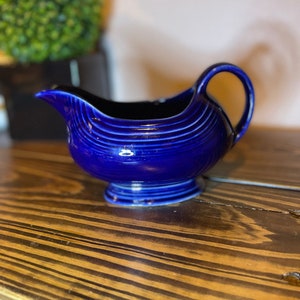 Puede incluir: Una jarra de crema de cerámica azul cobalto con un cuerpo redondeado y un pico acampanado. La jarra tiene un diseño acanalado y una base pequeña.