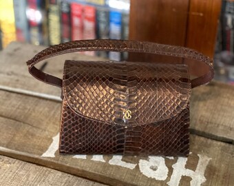 Peut inclure: Un petit sac à main en cuir marron avec un motif en peau de serpent. Le sac a un fermoir doré et une courte bandoulière.